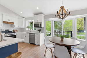 Kitchen with white cabinetry, stainless steel appliances, vaulted ceiling, hanging lights, and light stone counters