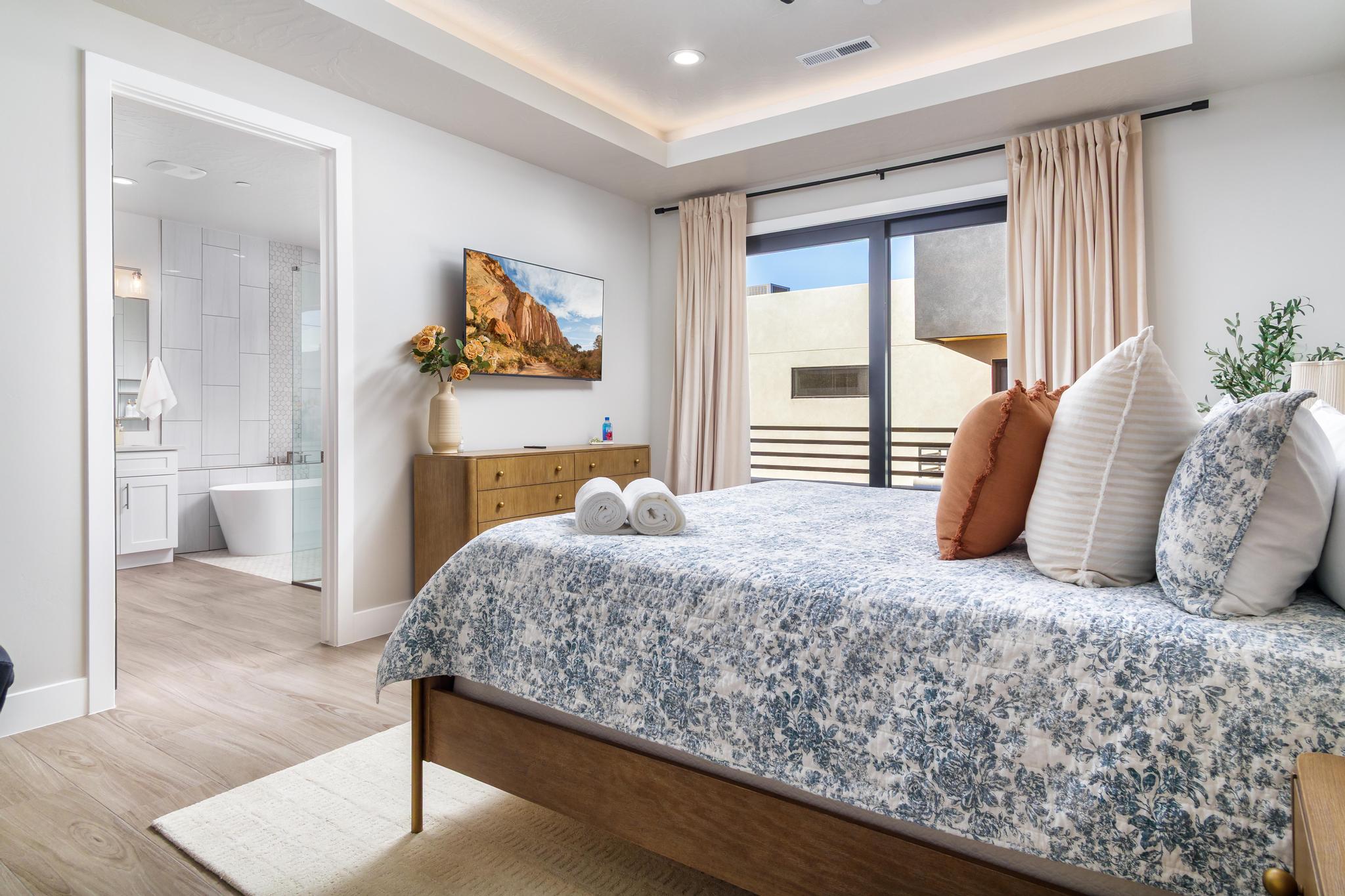Bedroom featuring access to exterior, a raised ceiling, light wood-style floors, recessed lighting, and connected bathroom