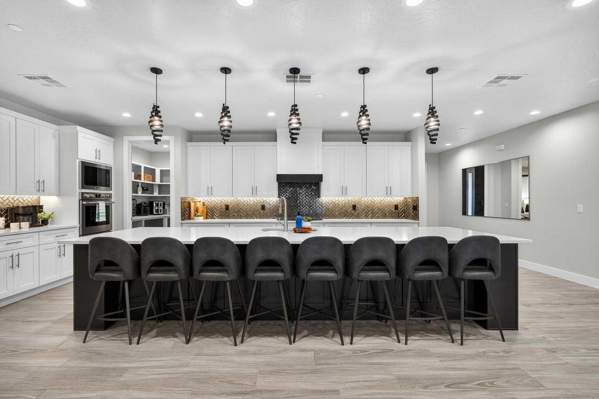 Dual tone kitchen with a breakfast bar, a large island with sink, backsplash, stainless steel appliances, and light wood-type flooring