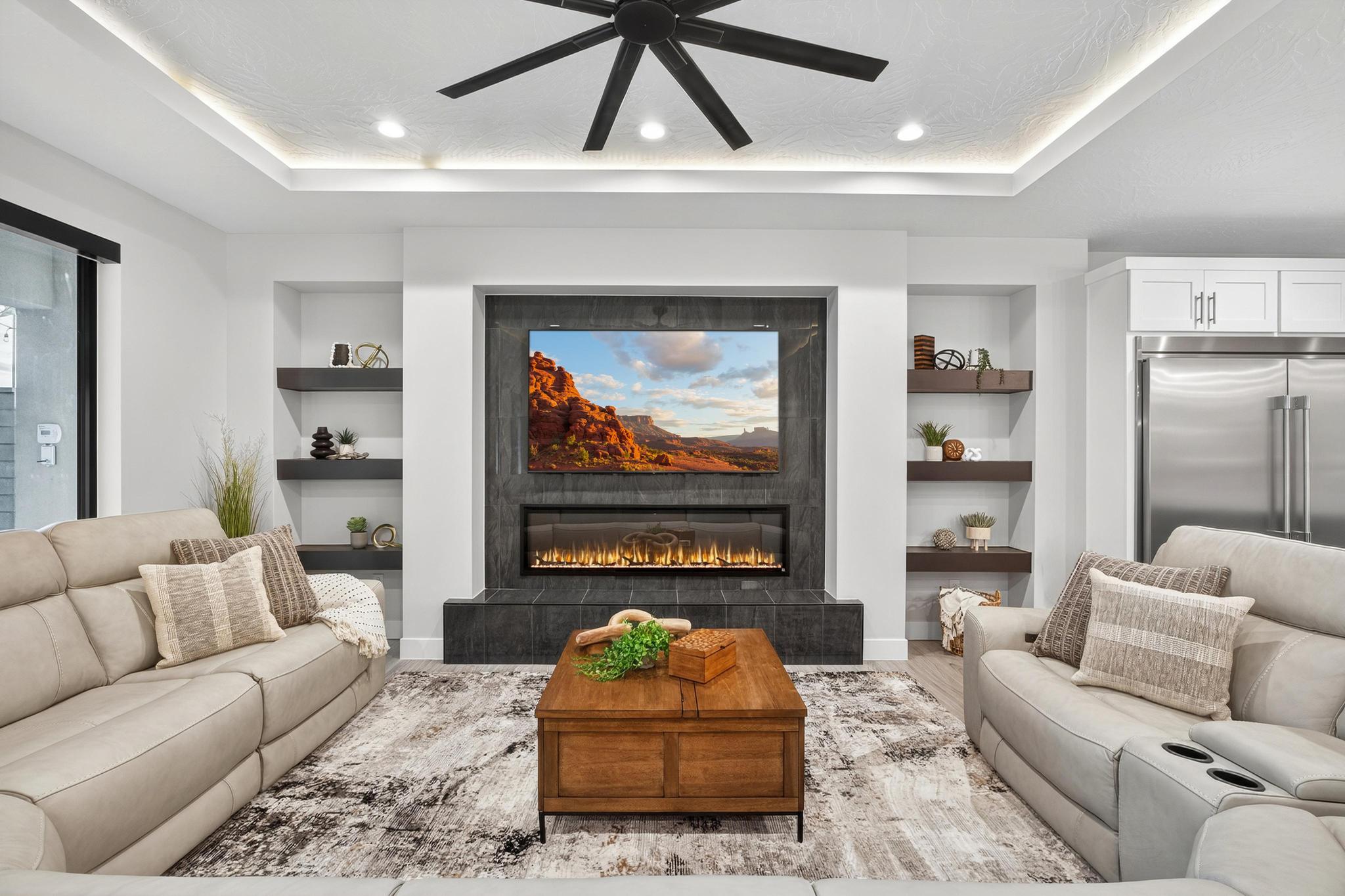 Living area with built in shelves, a ceiling fan, wood finished floors, a raised ceiling, and a tile fireplace