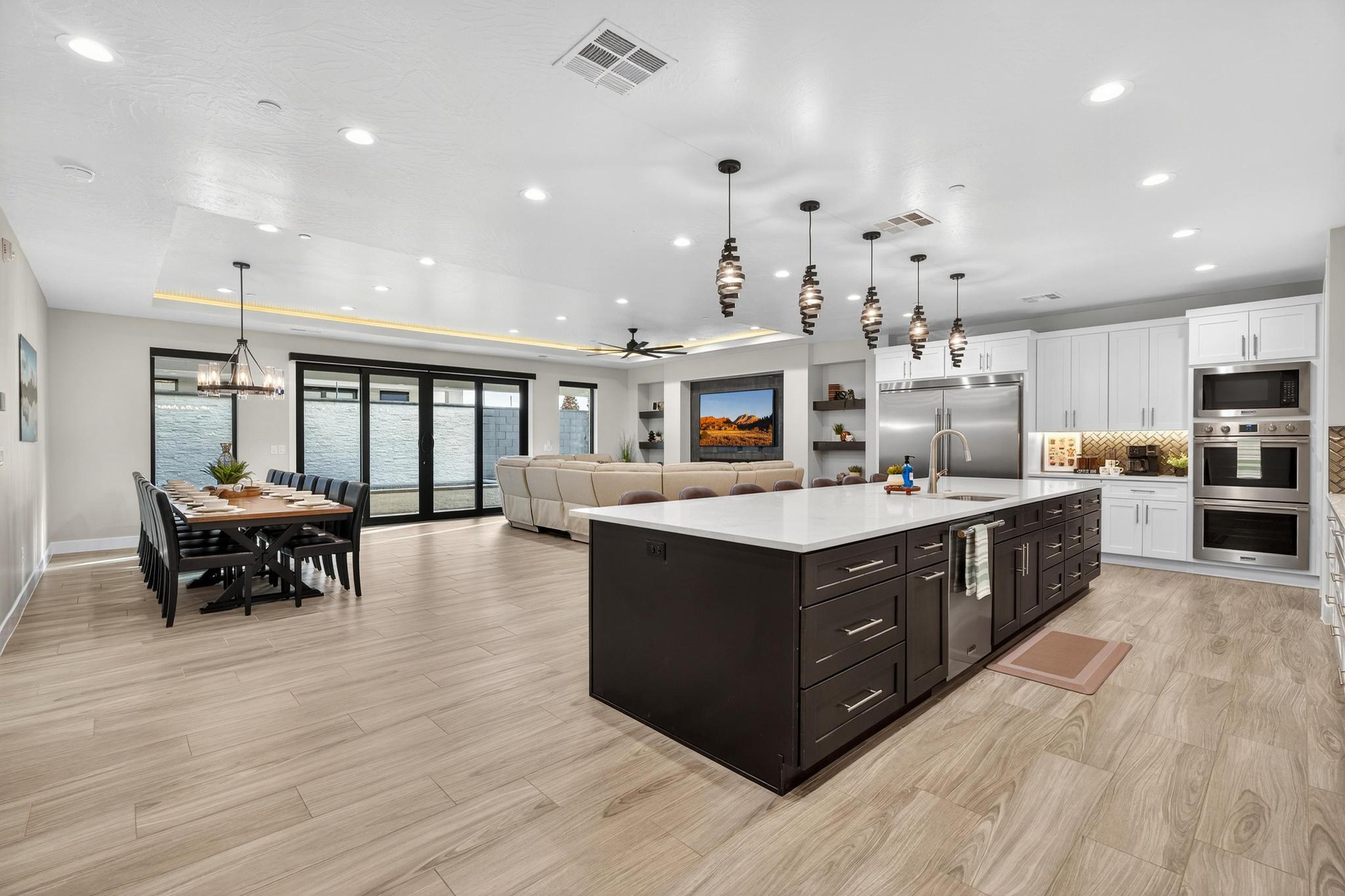 Kitchen with dual tone cabinetry, open floor plan, an island with sink, a ceiling fan, and built in appliances