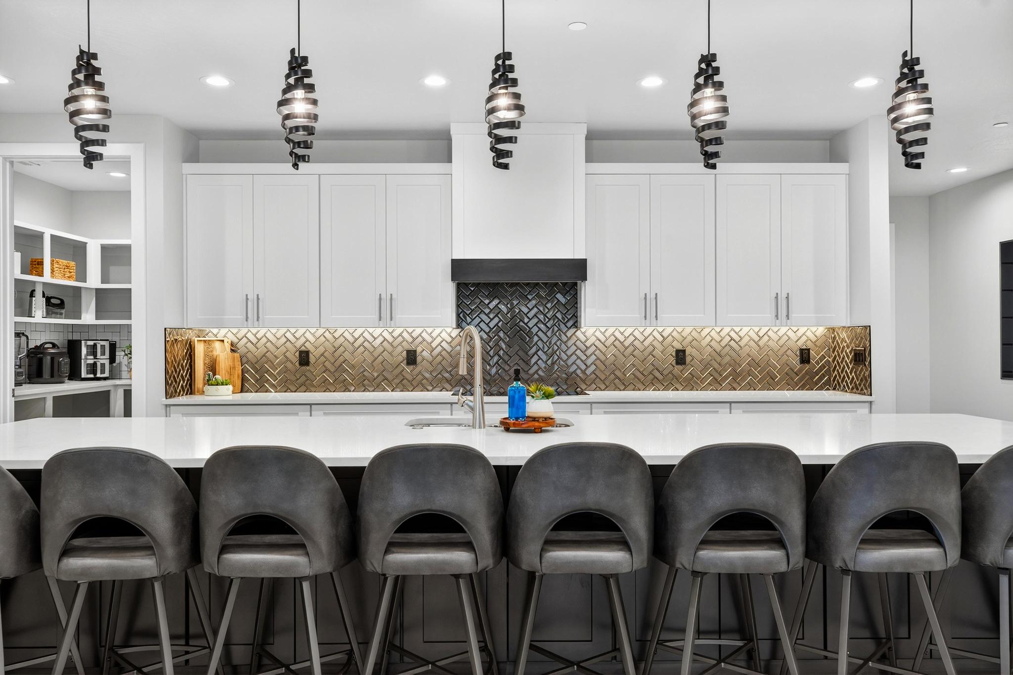 Two tone kitchen featuring a kitchen breakfast bar, hanging light fixtures, tasteful backsplash, light stone counters, and two tone cabinets