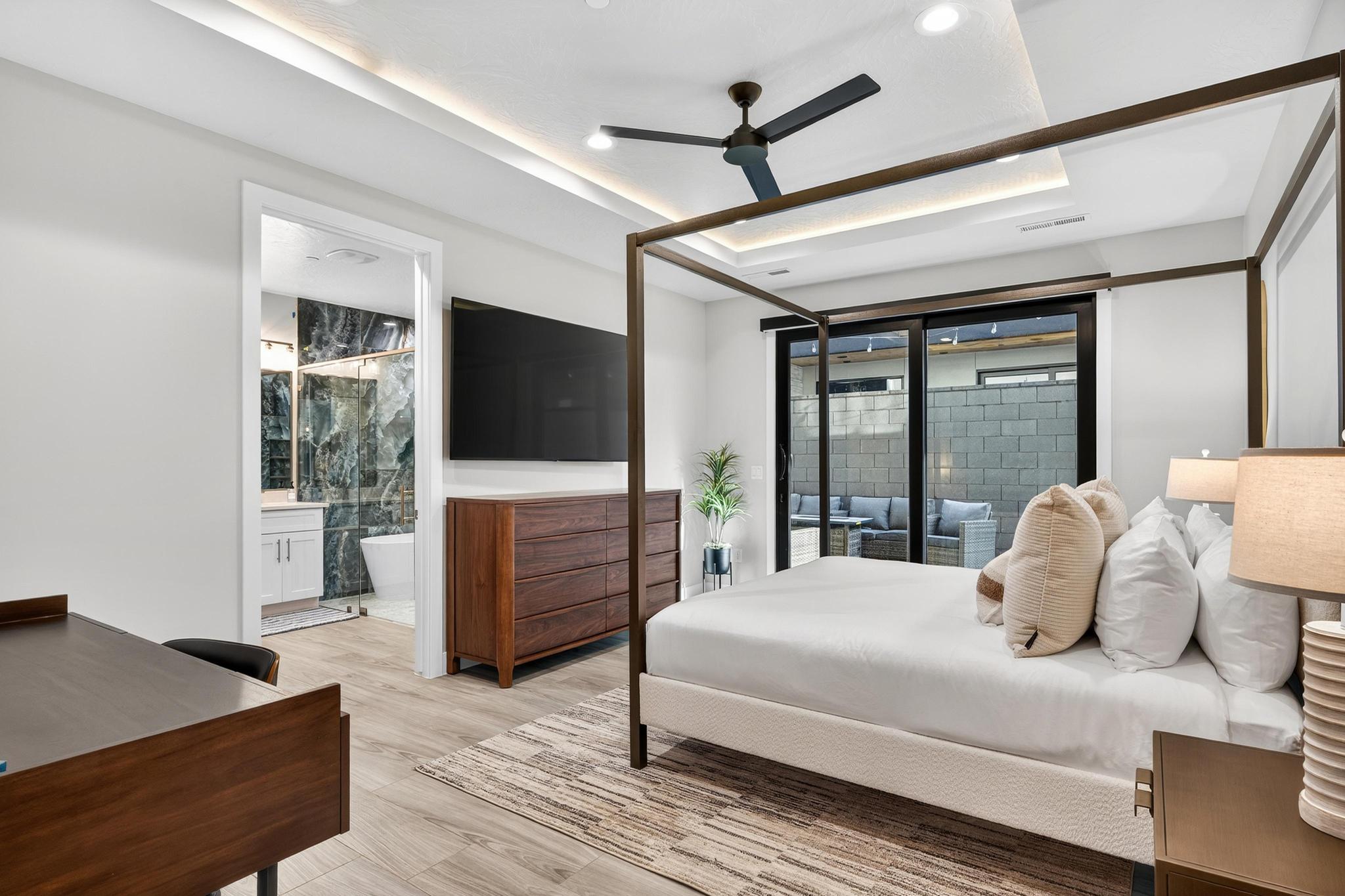 Bedroom featuring a tray ceiling, ceiling fan, access to exterior, light wood-style floors, and ensuite bathroom