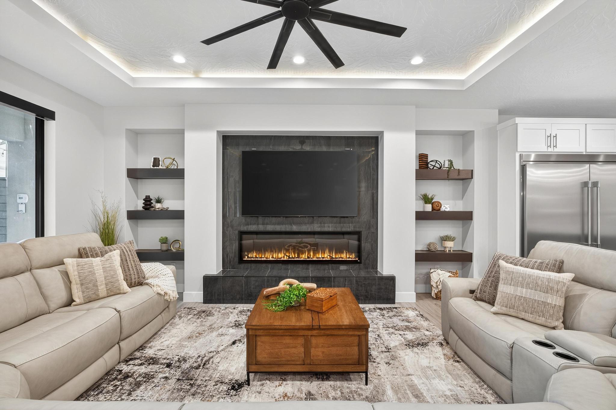 Living area with built in features, a ceiling fan, wood finished floors, a tray ceiling, and a tile fireplace
