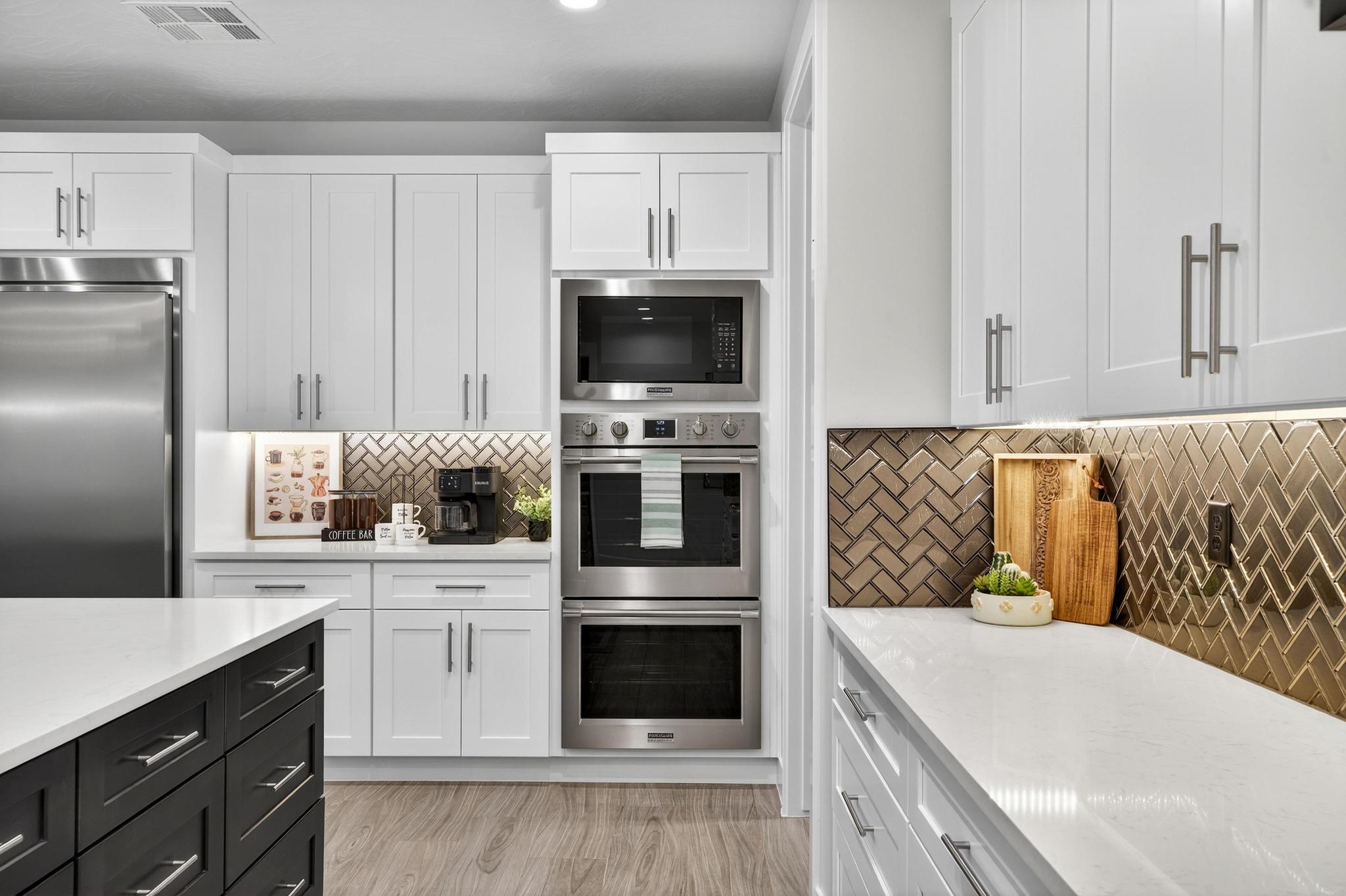 Dual tone kitchen featuring built in appliances, light stone countertops, two tone cabinets, light wood-style floors, and backsplash