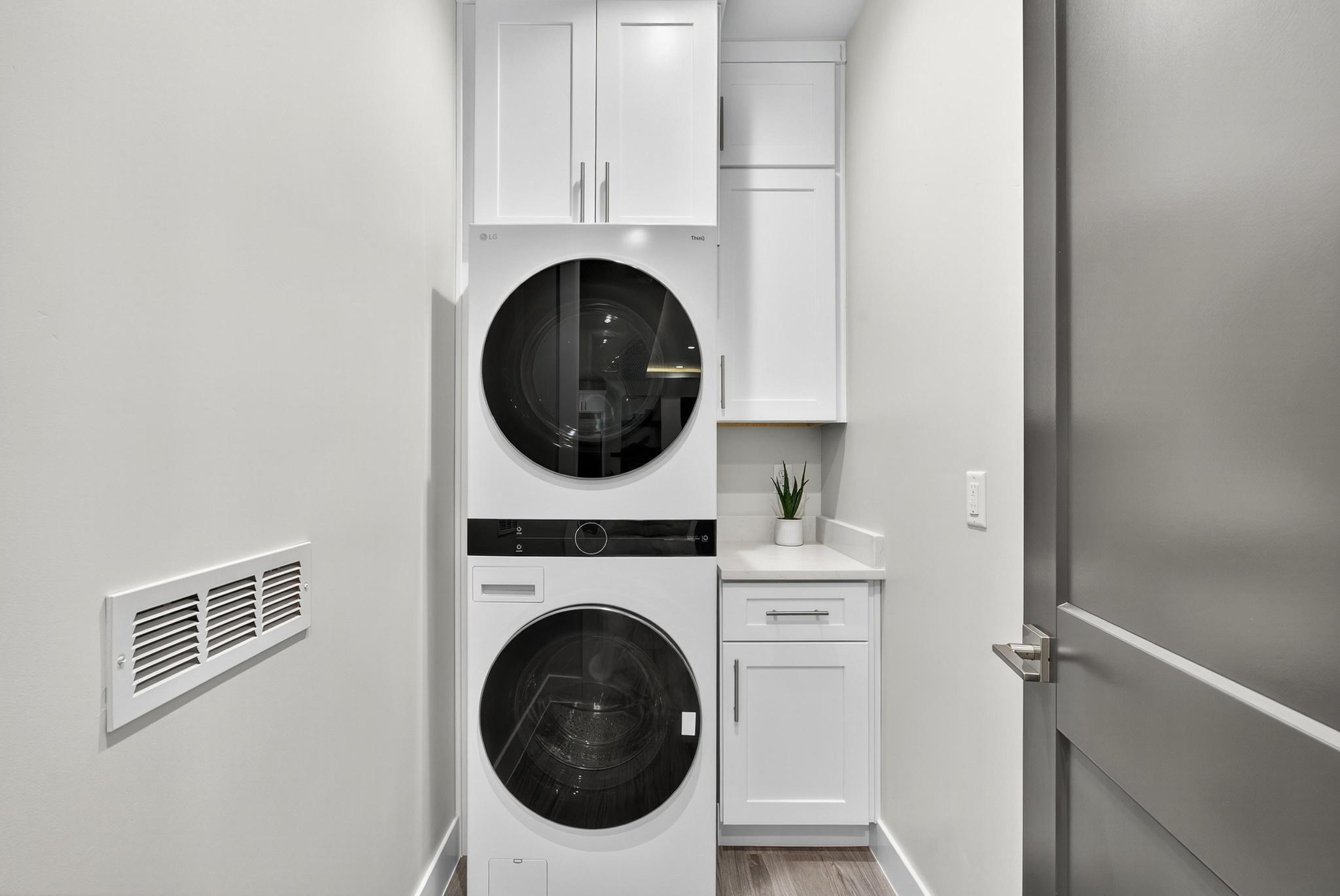 Laundry area with cabinet space, stacked washer and dryer, and light wood-style flooring