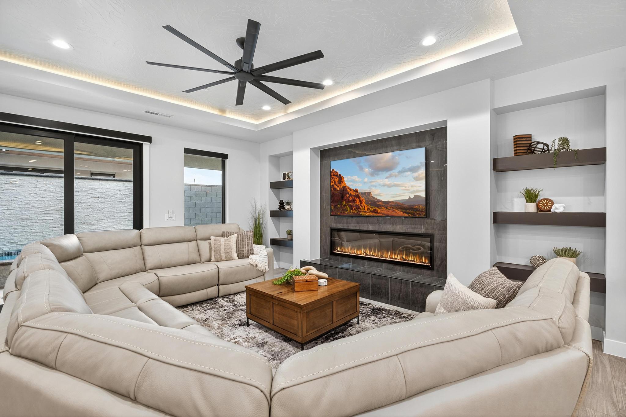 Living room with built in features, a tiled fireplace, a ceiling fan, wood finished floors, and recessed lighting