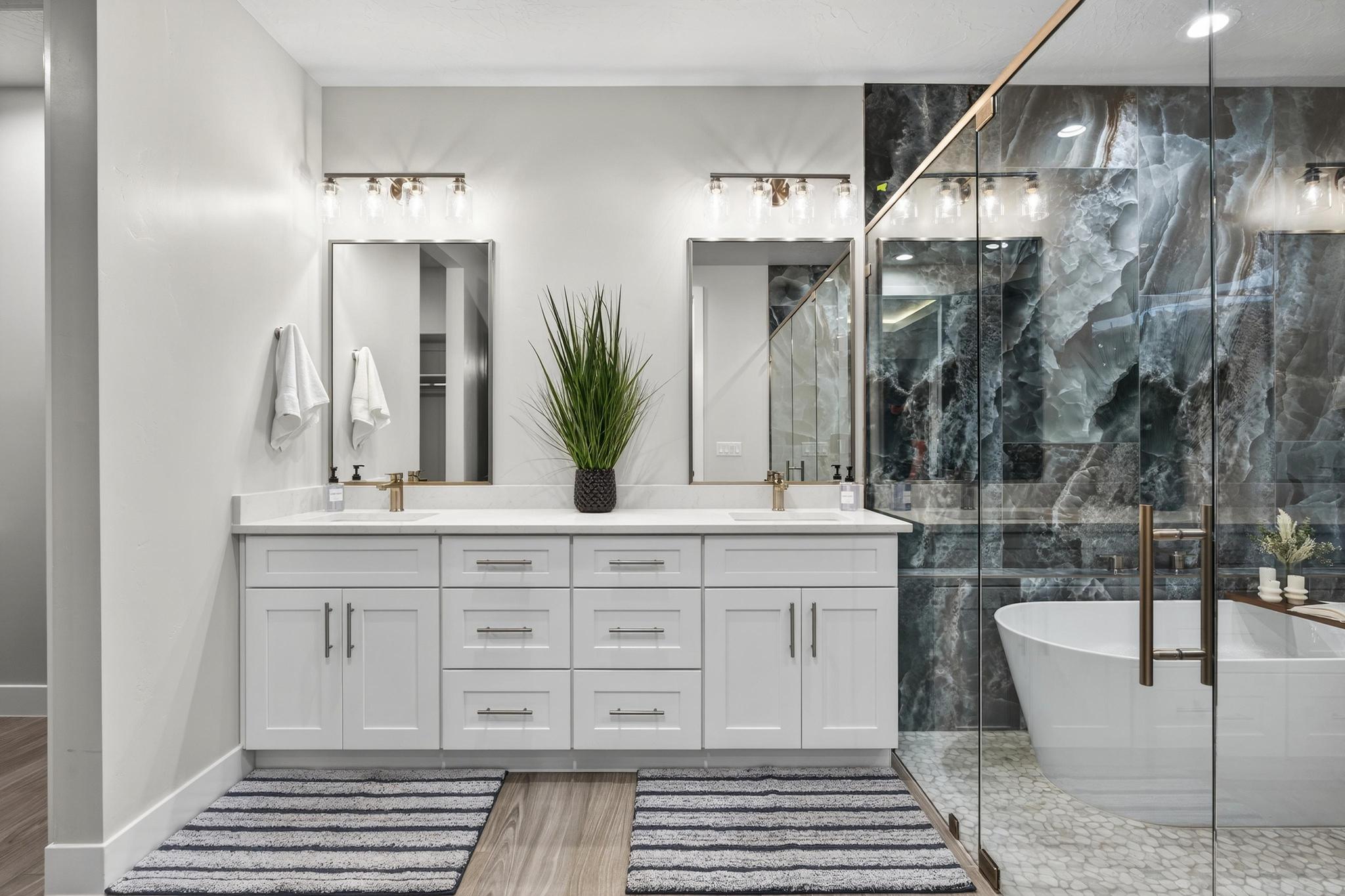 Full bath featuring double vanity, a freestanding bath, a marble finish shower, and light wood-style floors