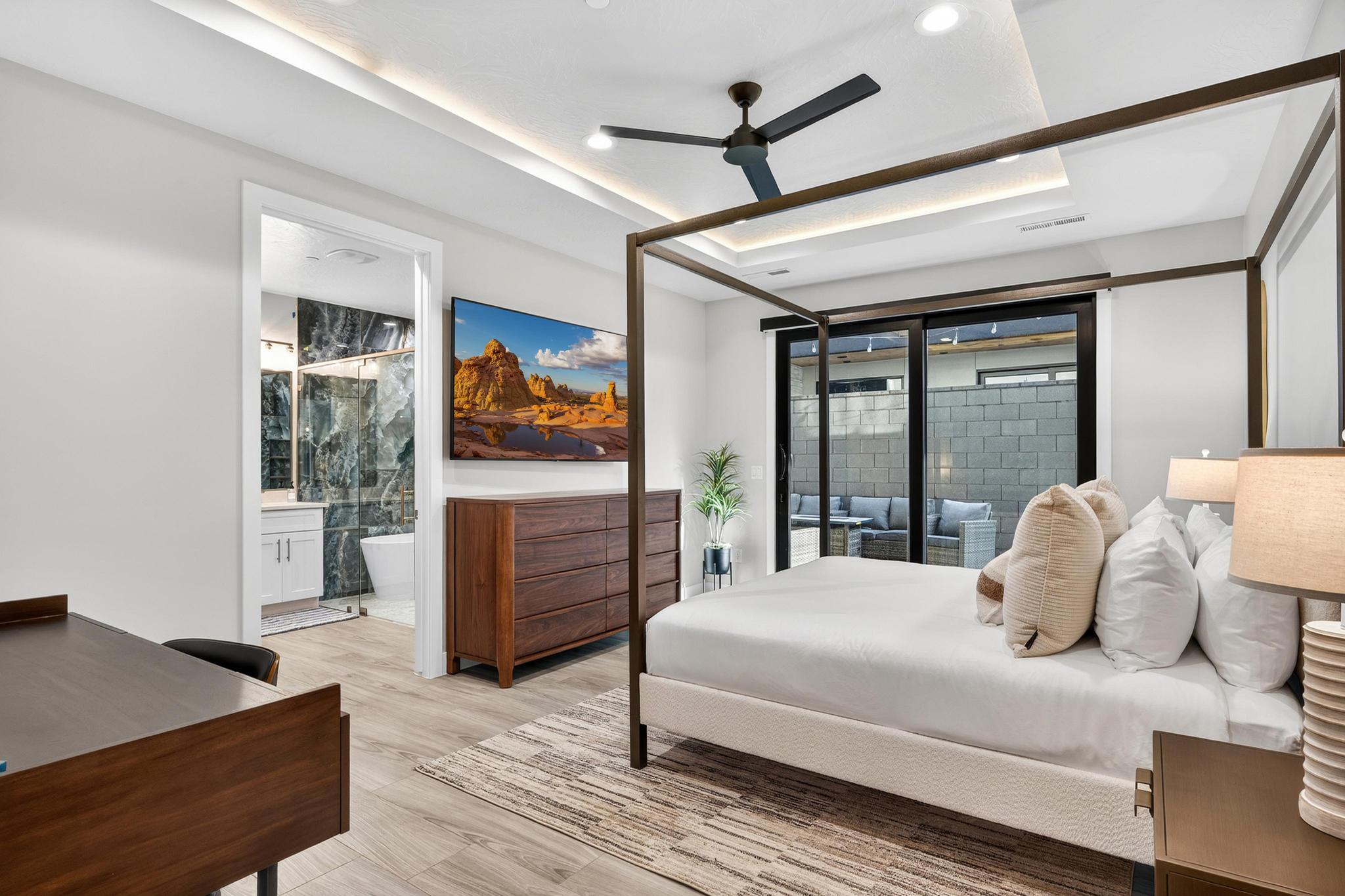 Bedroom with a ceiling fan, a raised ceiling, light wood-style flooring, access to outside, and ensuite bath