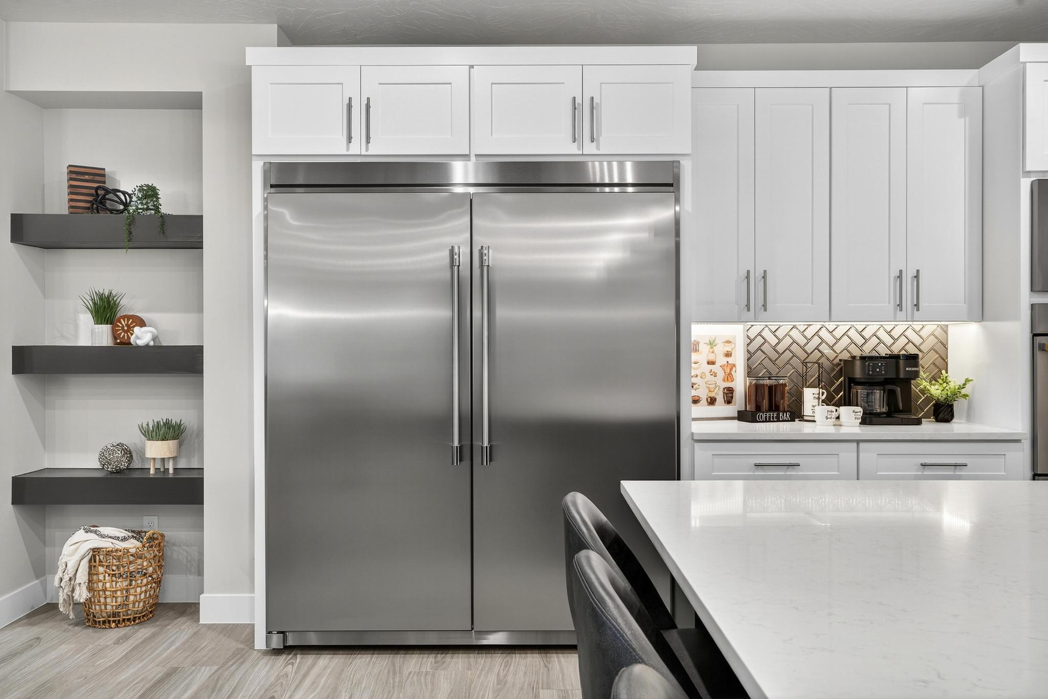 Kitchen with stainless steel built in refrigerator, white cabinets, light stone counters, and decorative backsplash