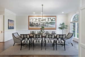 Expansive formal dining room featuring wainscoting, crown molding, wood flooring, and lovely chandelier.
