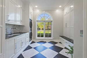 First laundry area with locker cabinet space, crown molding, stacked washer and dryer, space and recessed lighting