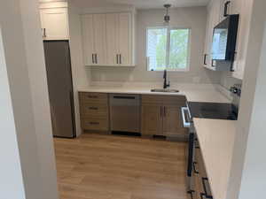 Two tone kitchen with stainless steel appliances, light stone counters, two tone cabinets, light wood finished floors, and decorative light fixtures