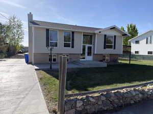 Raised ranch with brick siding, a chimney, and a patio area