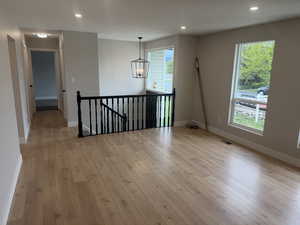 Empty room with light wood-style flooring and hanging lights