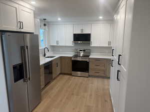 Kitchen with stainless steel appliances, two tone color scheme, light wood finished floors, light stone countertops, and pendant lighting