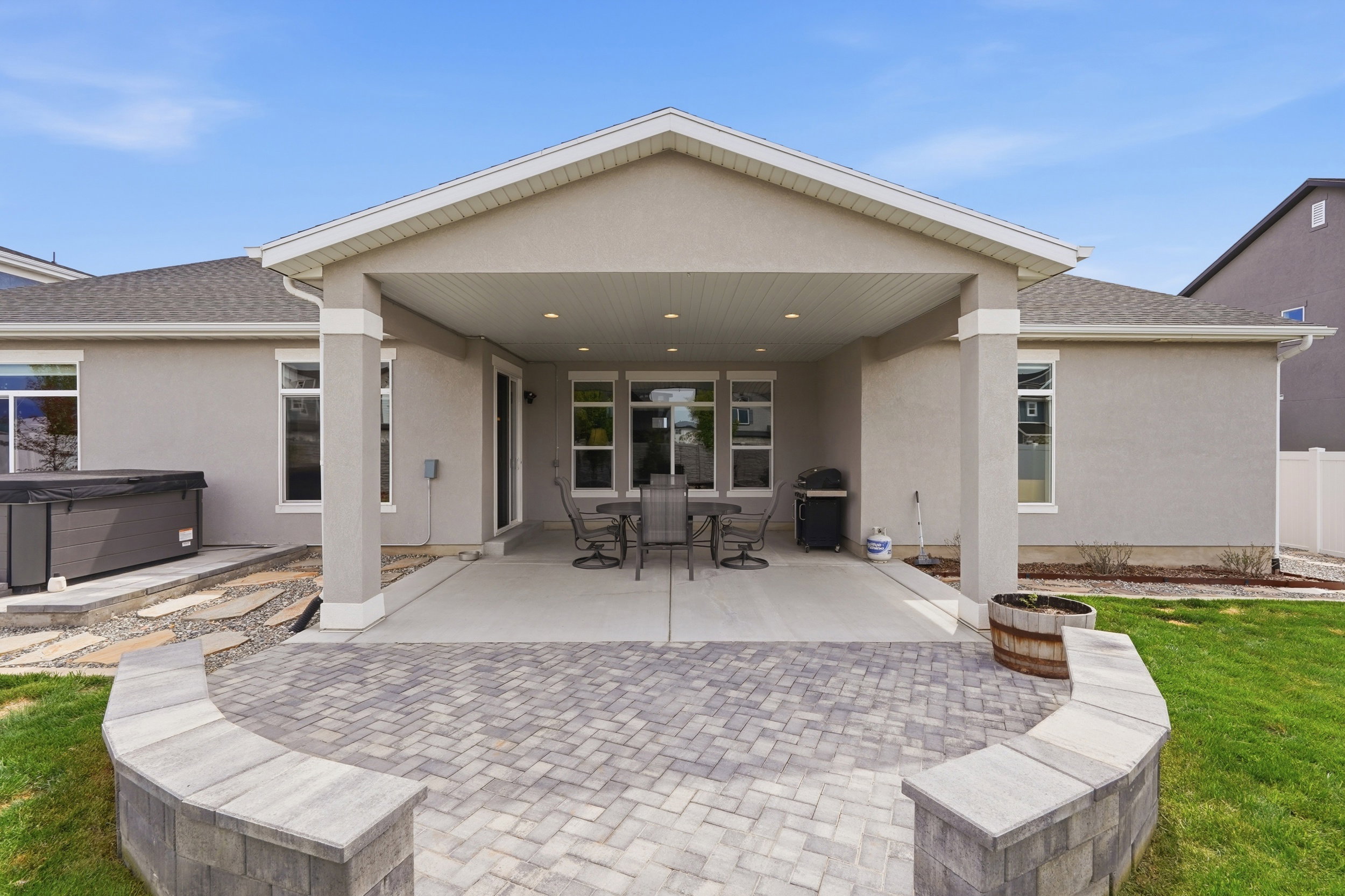 Back of house with stucco siding, outdoor dining area, a patio area, and a hot tub