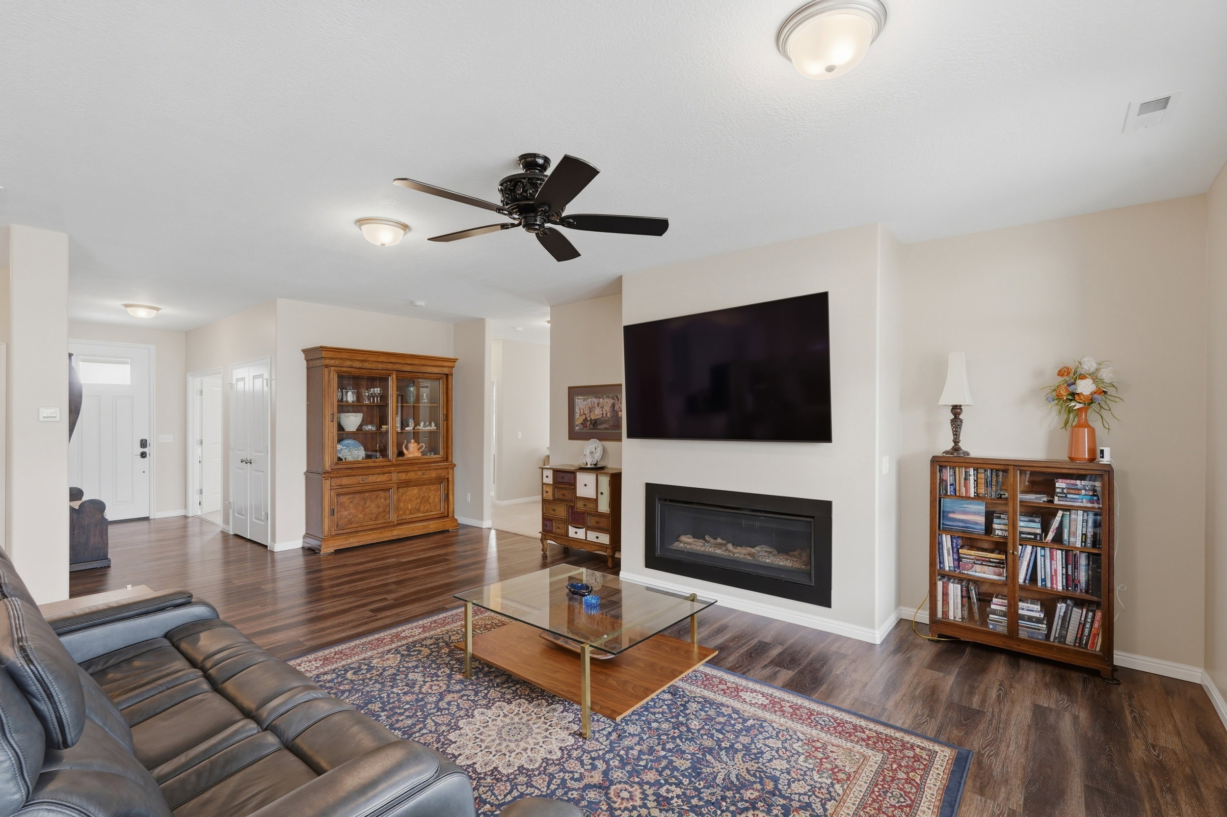 Living area featuring ceiling fan, a glass covered fireplace, and dark wood-type flooring