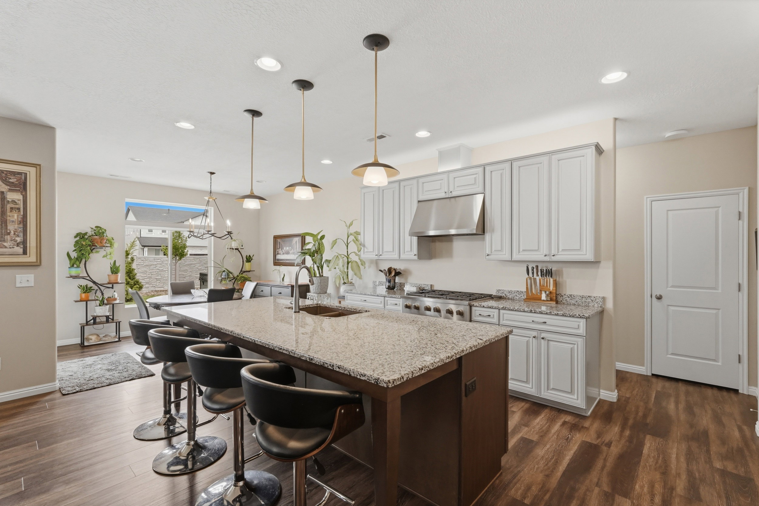 Kitchen featuring light stone counters, a kitchen bar, an island with sink, dark wood-style floors, and two tone cabinetry