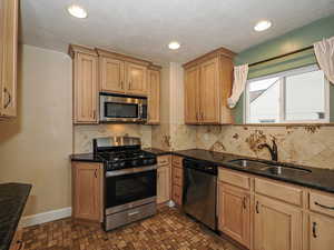 Kitchen with stainless steel appliances, dark stone counters, recessed lighting, and light wood finish cabinets