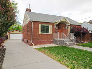 Bungalow-style home featuring a detached garage, an outbuilding, brick siding, a shingled roof, and a chimney