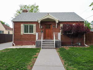 View of front of home with a chimney, brick siding, and roof with shingles