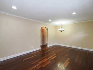 Spare room featuring arched walkways, dark wood-style floors, crown molding, and a chandelier