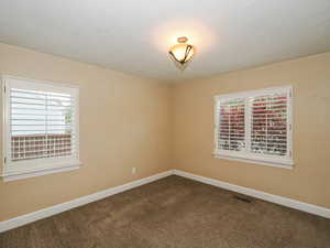 Empty room featuring dark carpet, a textured ceiling, and plenty of natural light