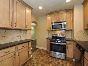Kitchen featuring stainless steel appliances, arched walkways, dark stone counters, recessed lighting, and backsplash