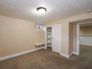 Unfurnished bedroom with dark colored carpet, a textured ceiling, a closet, and a wainscoted wall
