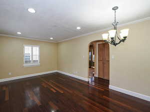 Unfurnished room with arched walkways, dark wood-style flooring, ornamental molding, and suspended lighting