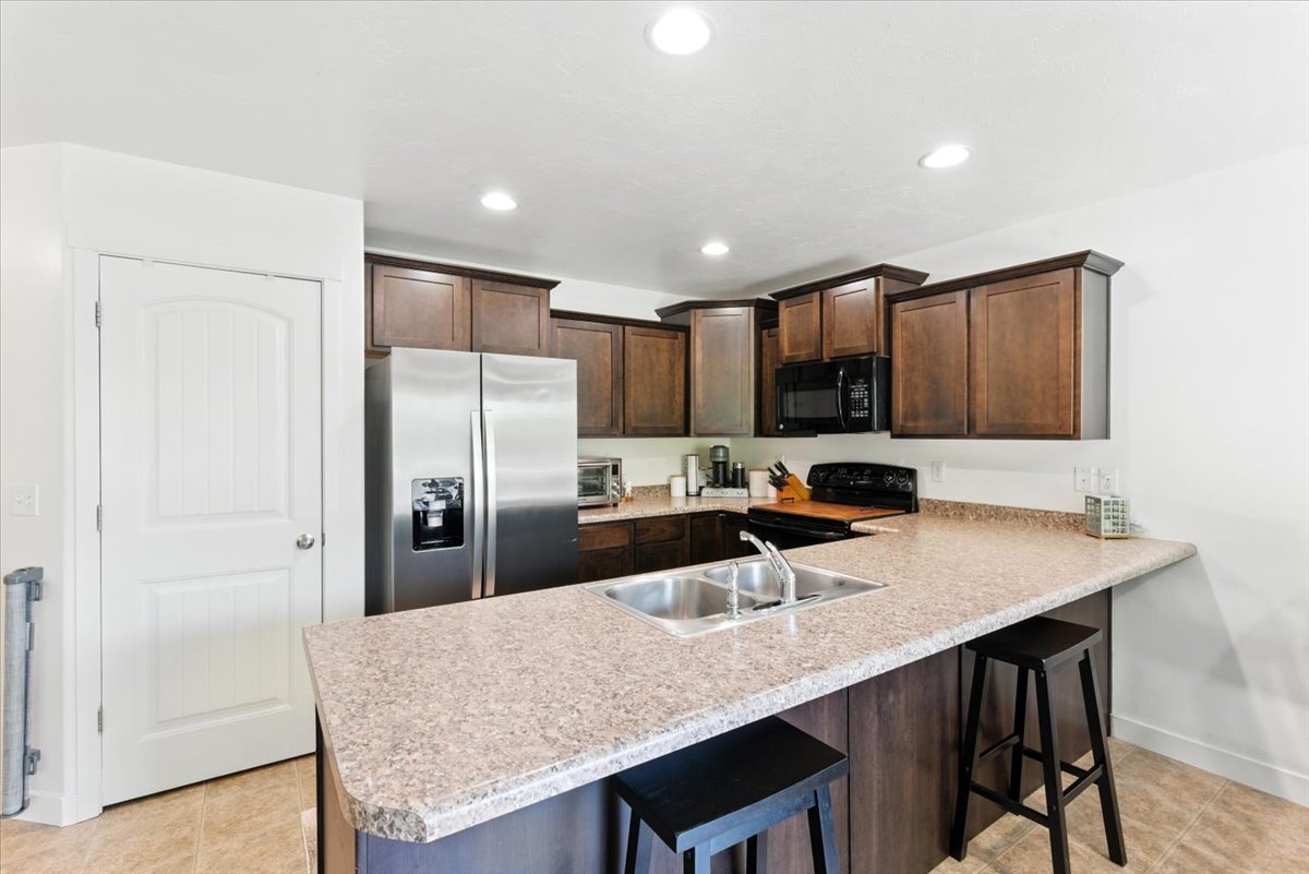 Kitchen with a kitchen breakfast bar, dark wood finish cabinetry, black appliances, a peninsula, and light countertops