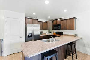Kitchen with a kitchen breakfast bar, dark wood finish cabinetry, black appliances, a peninsula, and light countertops