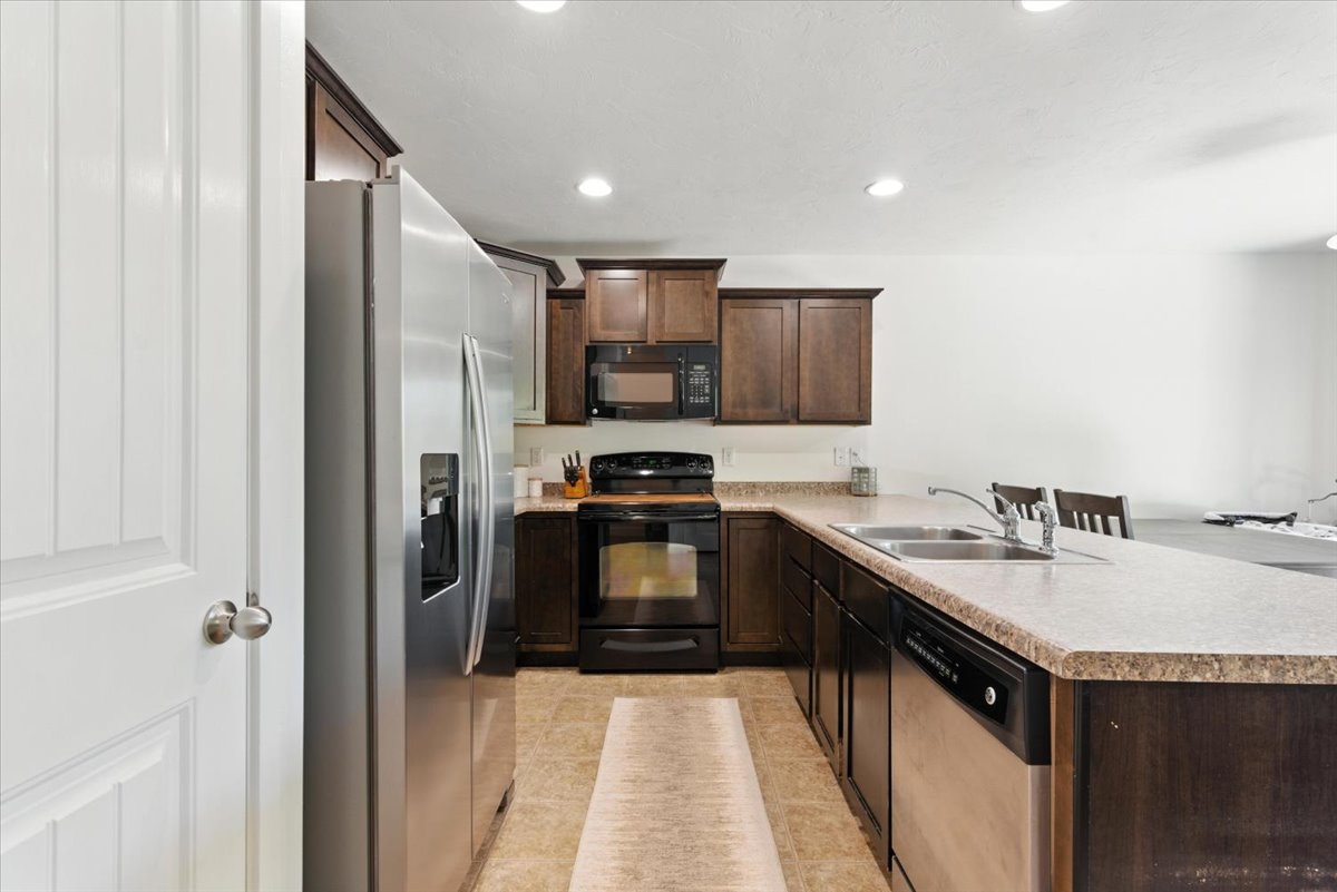 Kitchen featuring black appliances, dark wood finish cabinets, a peninsula, light countertops, and recessed lighting