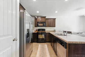 Kitchen featuring black appliances, dark wood finish cabinets, a peninsula, light countertops, and recessed lighting