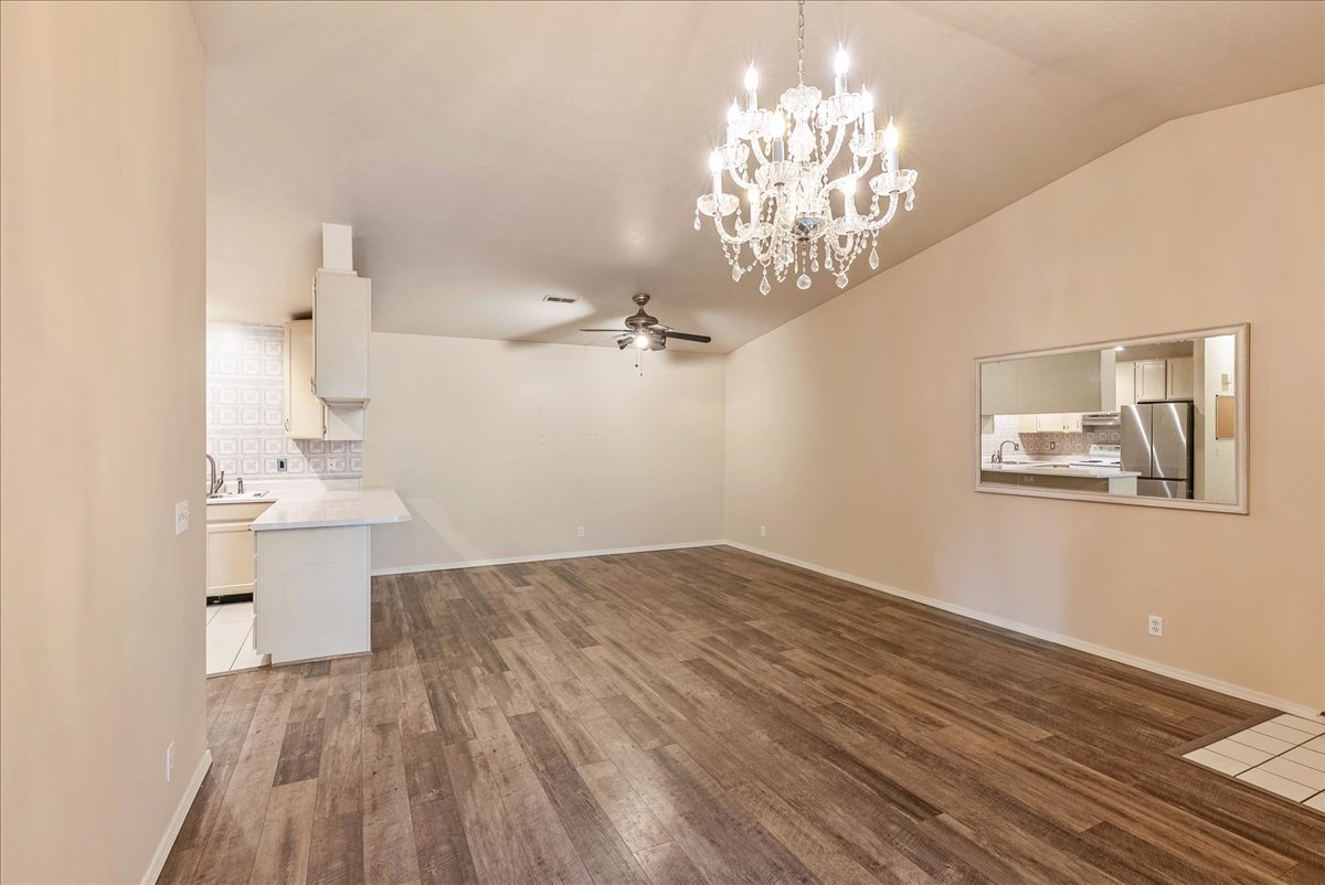 Unfurnished living room featuring dark wood-style floors, suspended lighting, a ceiling fan, and lofted ceiling