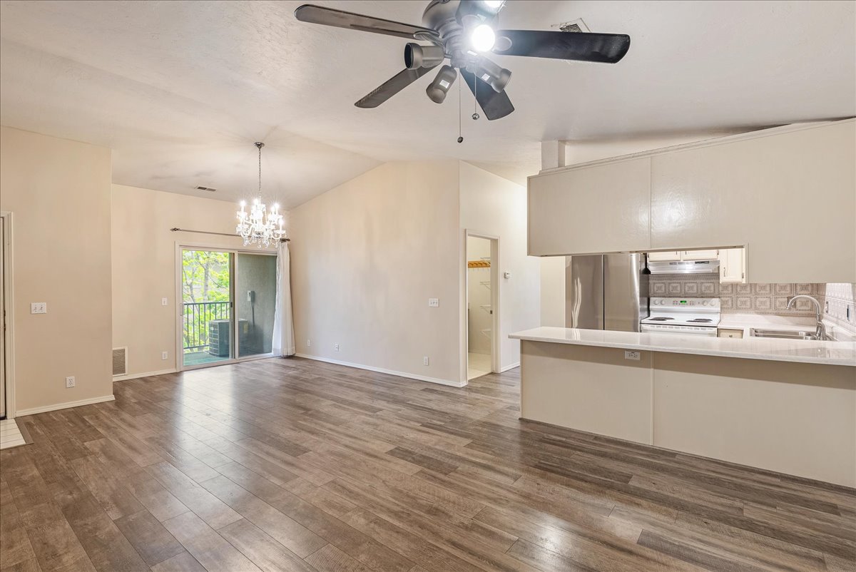 Unfurnished living room featuring lofted ceiling, ceiling fan, suspended lighting, and dark wood-style floors