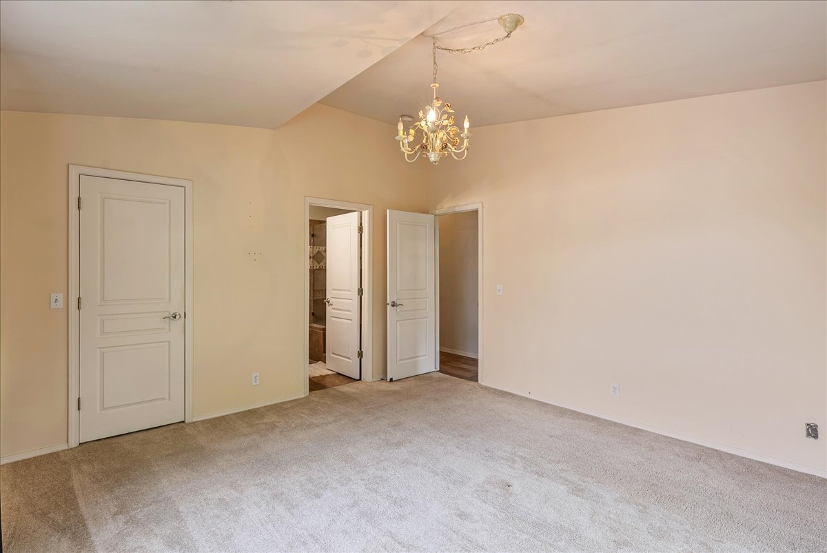Unfurnished bedroom with ensuite bathroom, suspended lighting, and light carpet