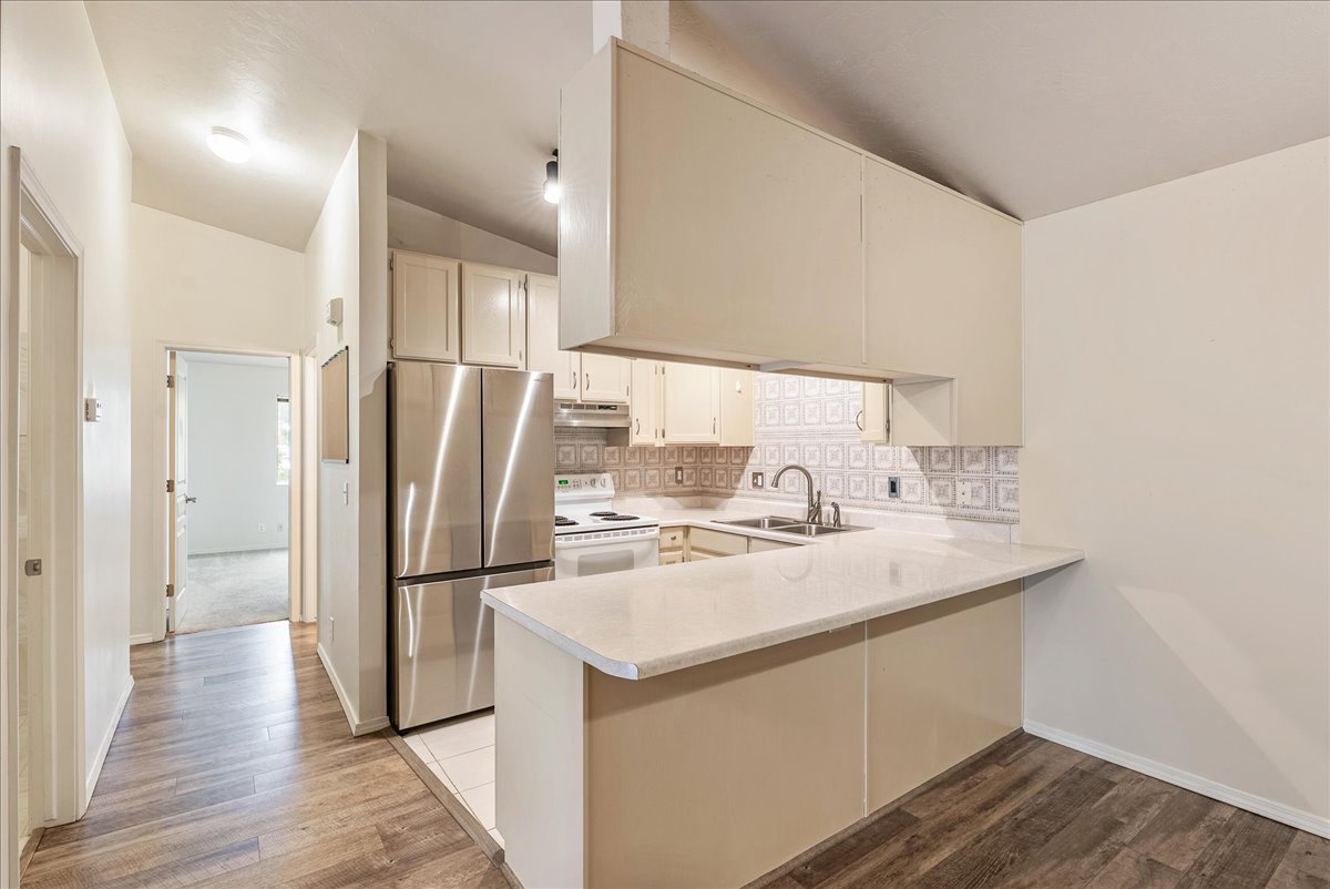Kitchen with light countertops, freestanding refrigerator, a peninsula, lofted ceiling, and electric range