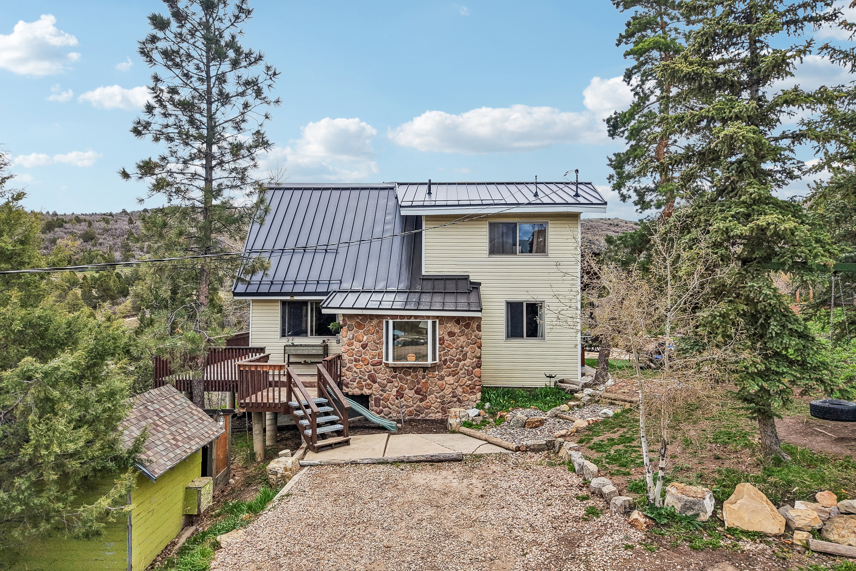 Rear view of property with a standing seam roof, stone siding, a playground, a wooden deck, and a patio