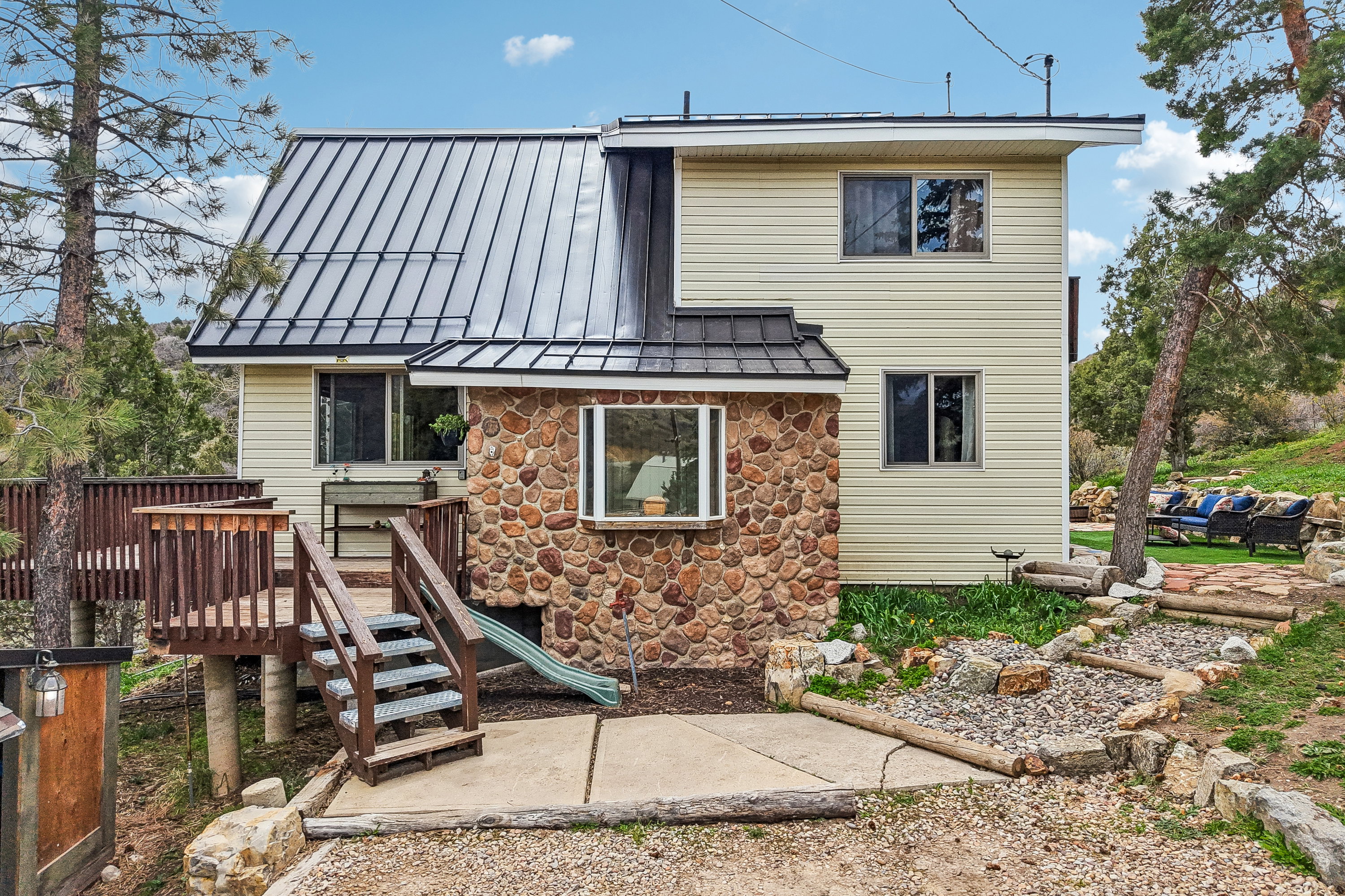 Rear view of property featuring a standing seam roof, stone siding, and a patio area