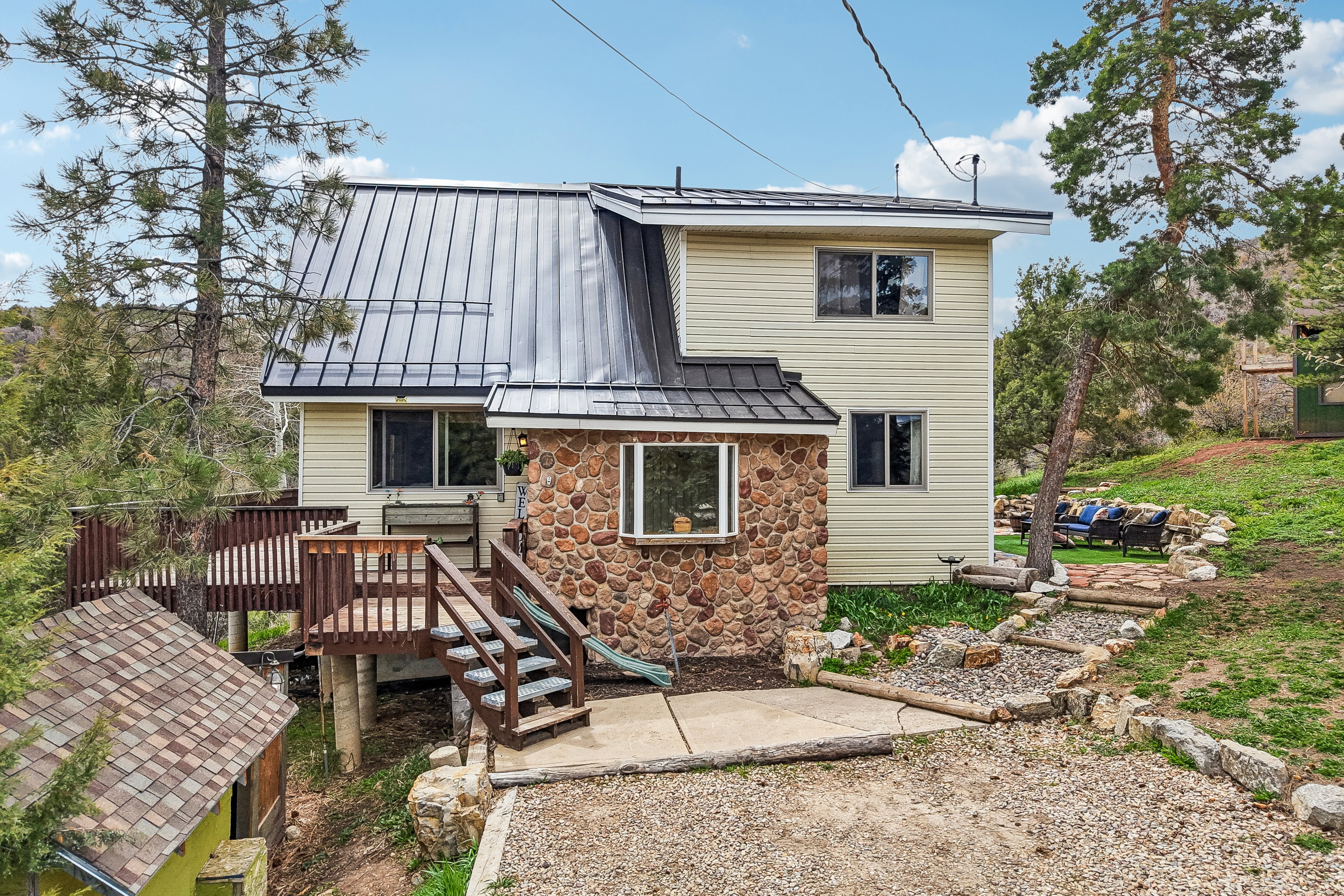 Back of house featuring a standing seam roof, stone siding, a patio area, and a deck