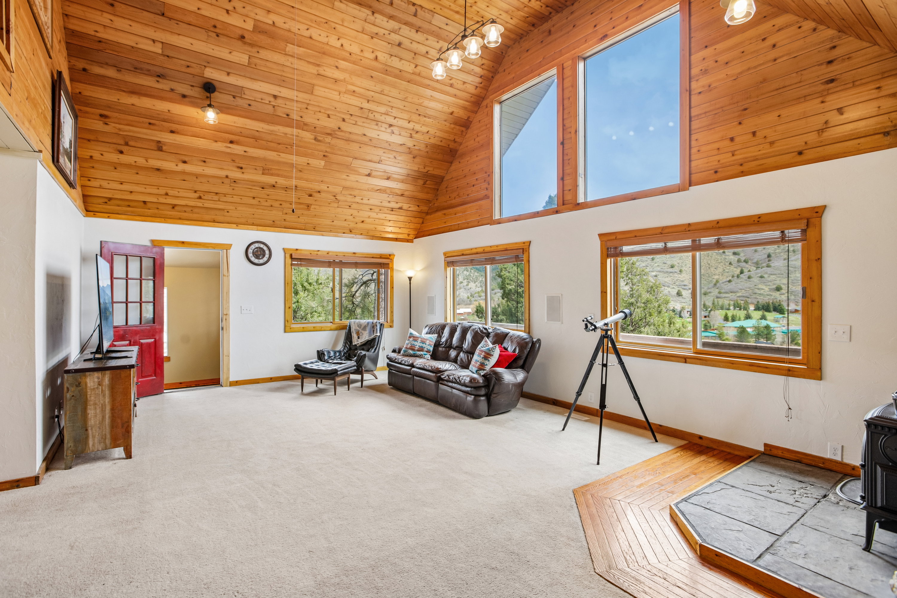 Living area featuring a vaulted wooden ceiling, light colored carpet, and a wood stove