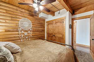 Bedroom featuring a wooden ceiling with exposed beams, a closet, ceiling fan, log walls, and wood finished floors