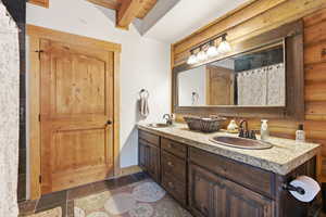 Bathroom with double vanity, a shower with shower curtain, beamed ceiling, and wood walls
