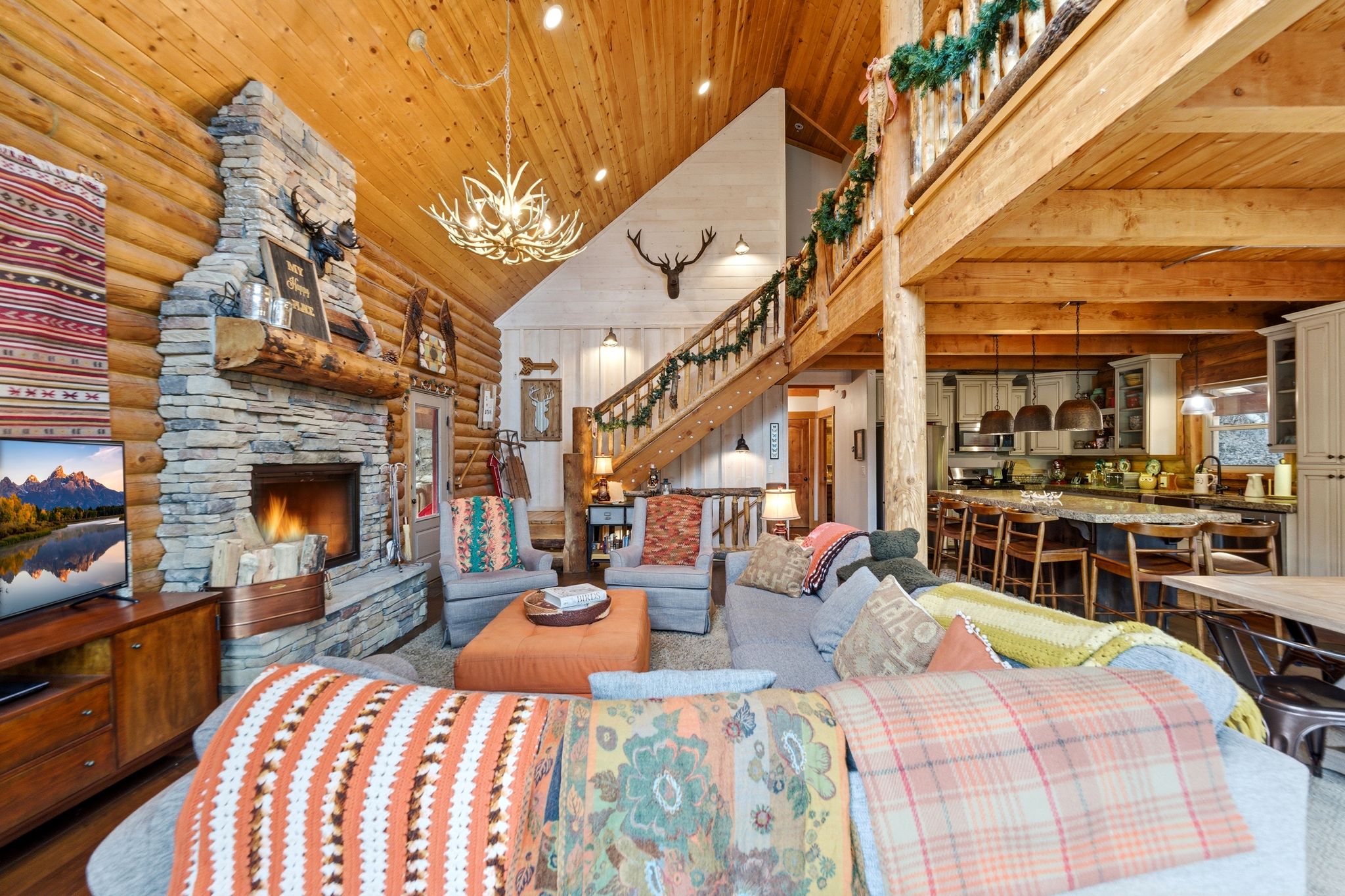 Living area with a vaulted wood ceiling, a stone fireplace, rustic walls, and hanging lights
