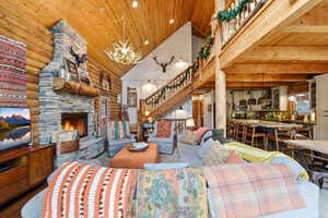Living area with a vaulted wood ceiling, a stone fireplace, rustic walls, and hanging lights