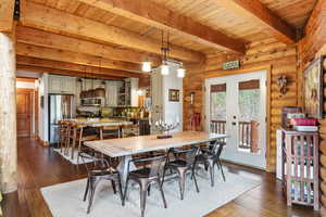 Dining space featuring french doors, dark wood-style floors, rustic walls, and a wooden ceiling with exposed beams