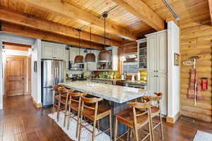 Kitchen featuring stainless steel appliances, pendant lighting, dark wood finished floors, light stone counters, and rustic walls