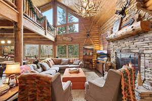 Living room featuring a vaulted wood ceiling, a fireplace, suspended lighting, rustic walls, and wood finished floors